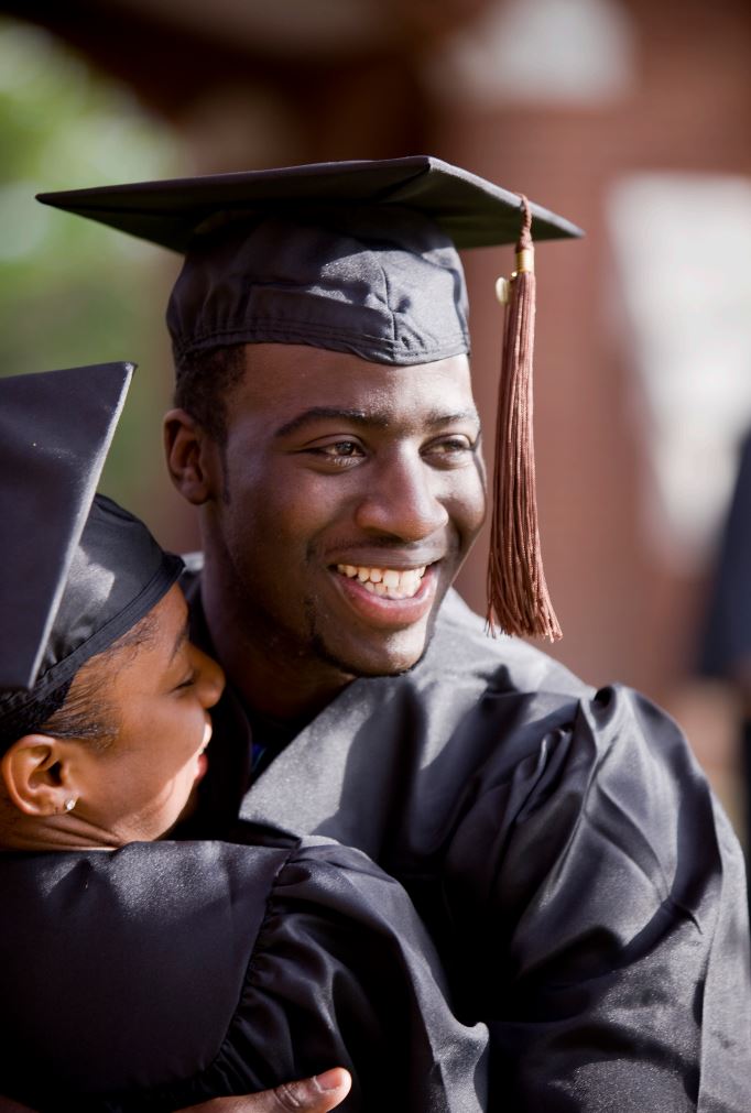 Two students, laughing, smiling, and hugging on graduation day