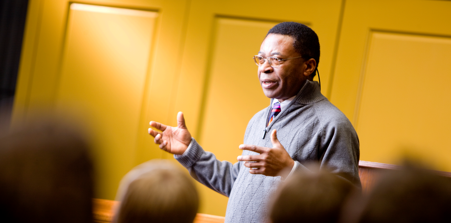 A Professor gestures with his hands as he teaches a group of students