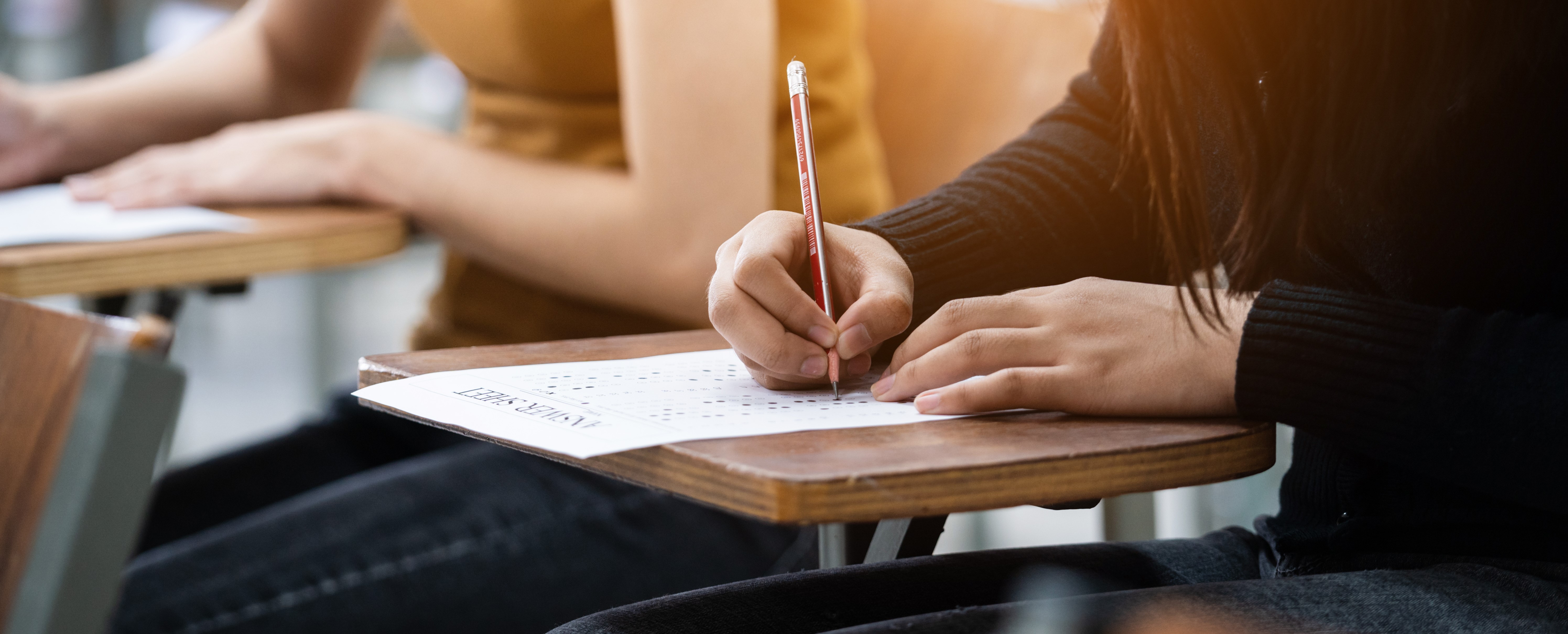 photo of students testing focused on one student's desk as they are writing on their exam