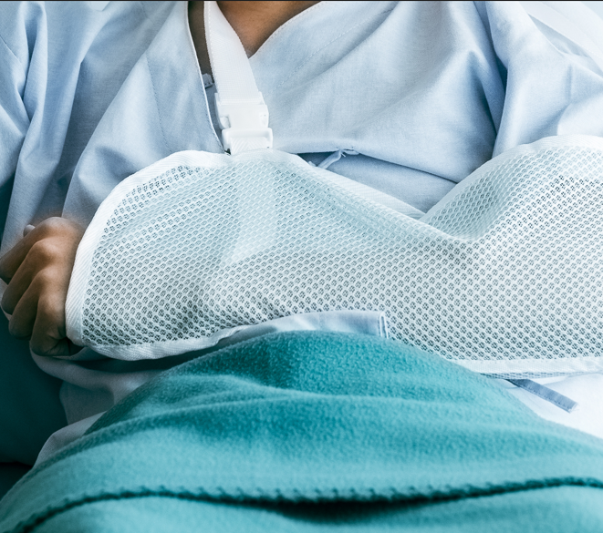 Photo of a person's arm in cast/sling as they sit in a hospital bed