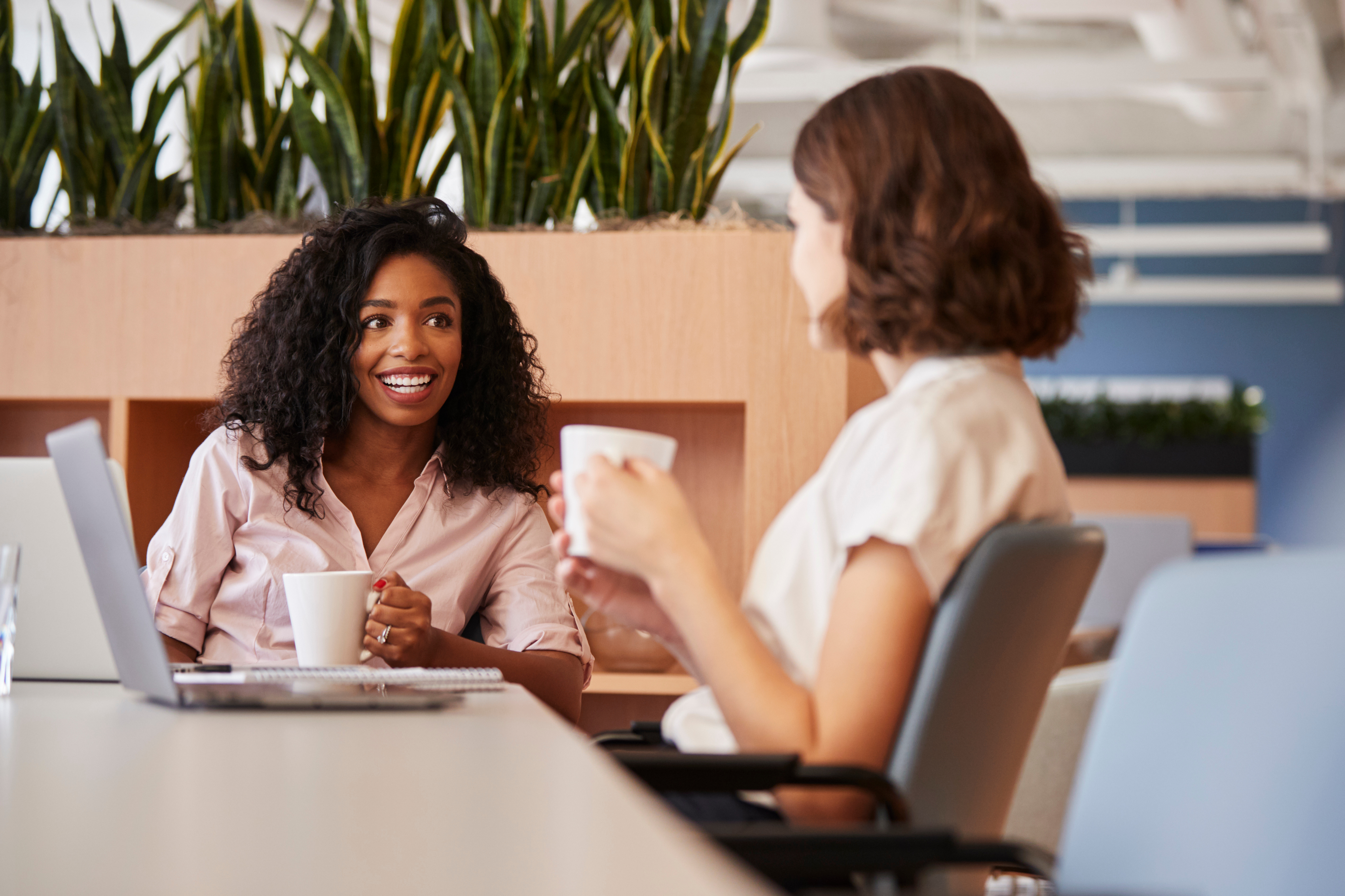 Two women sitting across a table from eachother, smiling