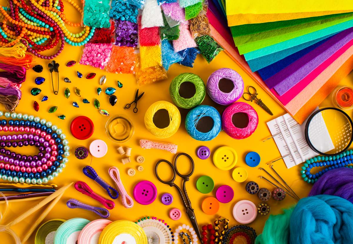 Top down view of a yellow table full of colorful craft items like string, paper, scissors, buttons and more