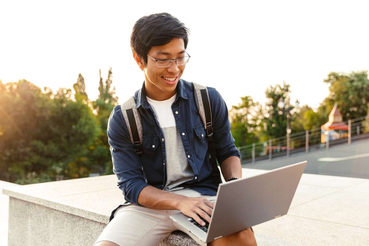 Photo of a man sitting on a cement ledge outside on his laptop smiling