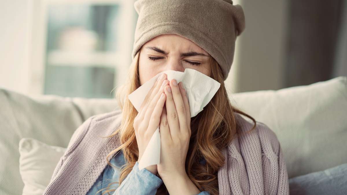 Photo of girl with a hat and blanket around her shoulders, sneezing into a tissue.