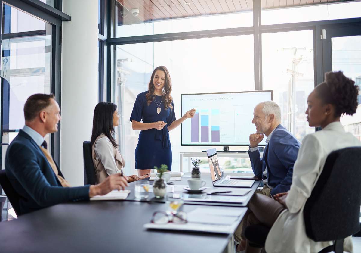 Female presenting in an office with large windows and a projector screen to a group of professionals