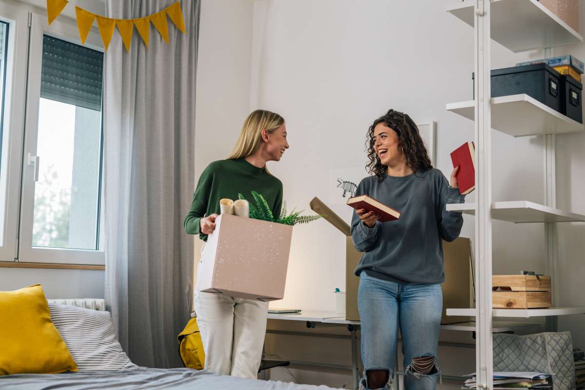 two college students in an empty dorm smiling and laughing unpacking boxes