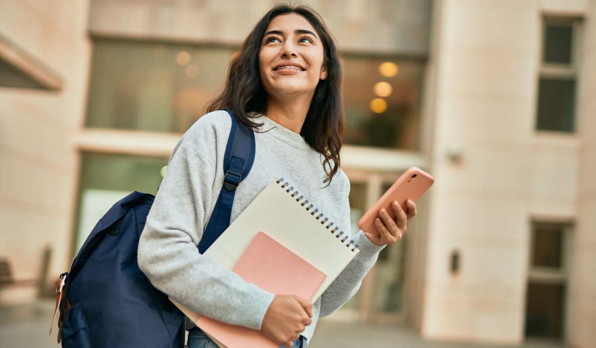 Female college student looking off into the distance, smiling, holding notebooks with a backpack